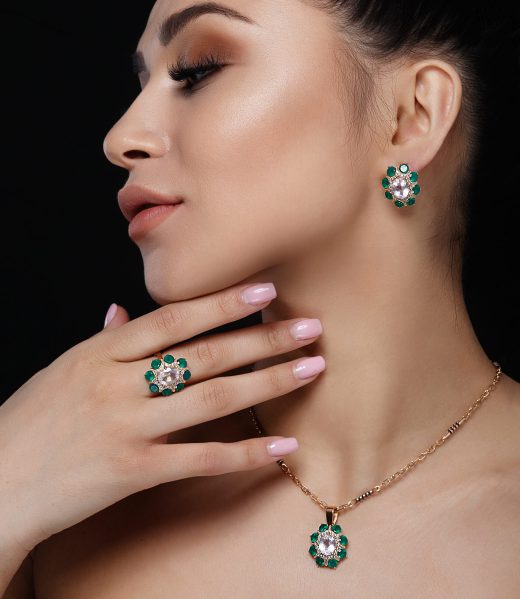 Charming model with dark hair shows rich golden earrings, necklace, and ring with green precious stones